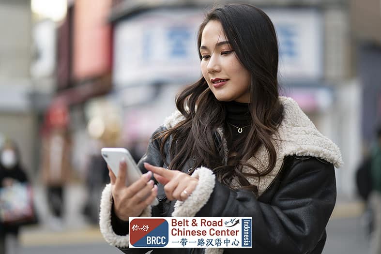 Remaja Asia menggunakan smartphone dengan aplikasi translate Mandarin otomatis di kota