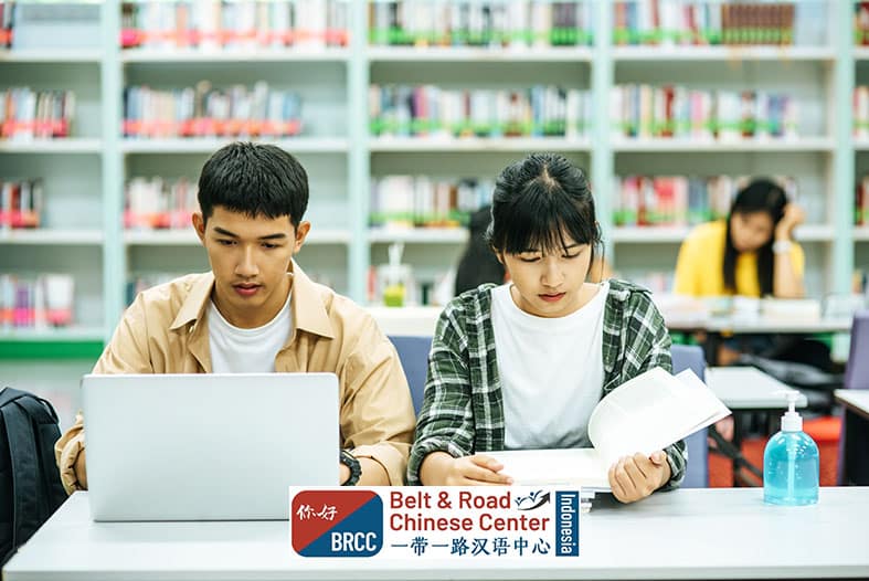 Mahasiswa perempuan membaca buku dan mahasiswa laki-laki menggunakan laptop di perpustakaan universitas Tiongkok